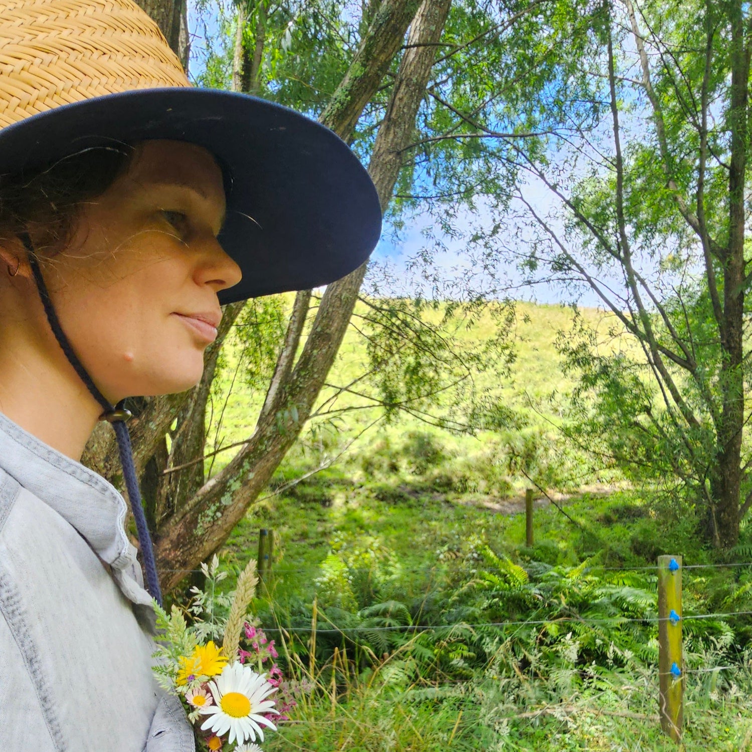 Person wearing a wide-brimmed hat in a natural setting with trees and greenery.